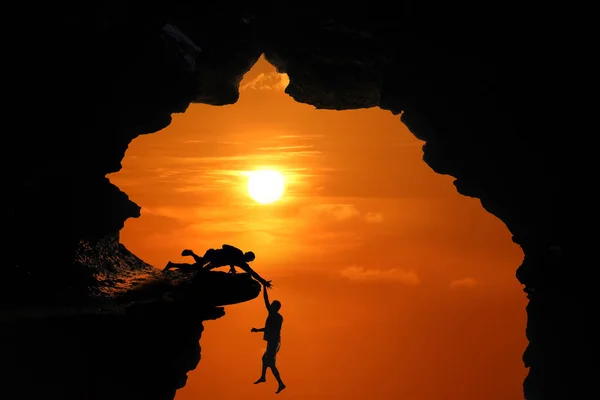 Silhuett av människan klättring i grottan eller höga klippor vid en röd s — Stockfoto