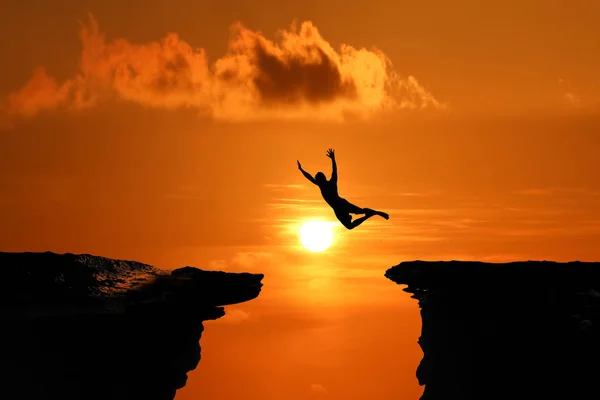 Silhouet van mannen zijn sprong tussen hoge klif op een rode hemel zon — Stockfoto