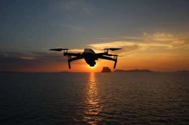 Gün batımında gökyüzünde uçarken drone'lar, Okyanus ve ada arka