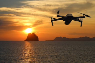 Gün batımında gökyüzünde uçarken drone'lar, Okyanus ve ada arka