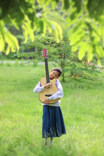 Азіатські дівчата школи грати на гітарі на галявині, студент вчитися — стокове фото