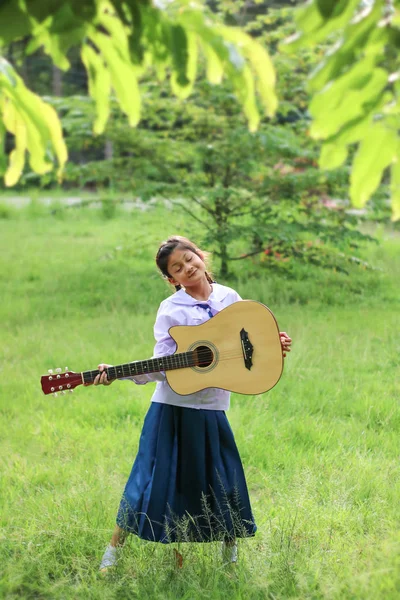 Азіатські дівчата школи грати на гітарі на галявині, студент вчитися — стокове фото