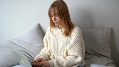 Süveter ve kot pantolonlu, dizüstü bilgisayarlı ve arkadaşlarıyla mesajlaşan mutlu genç bir kadın. Çevrimiçi öğrenim, çalışma, gezinme, kablosuz internet, teknoloji konsepti