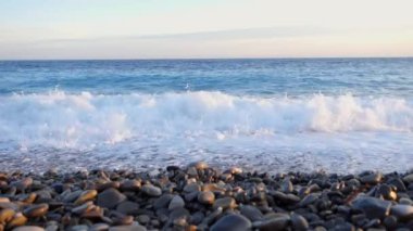 Deniz dalgaları ve arka planda gün batımıyla pürüzsüz ve temiz bir çakıl taşı plajı. Seyahat ve tatil kavramı.