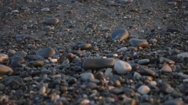 Pürüzsüz ve temiz çakıl taşları plajı ve arka planda köpüklü deniz dalgaları. Akdeniz kıyısından günbatımı video görüntüleri. Rahatlama, sakinlik ve tatil konsepti.