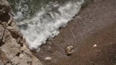 Kıyıdaki kayalık kumsal çakıl taşlarının ve dalgalı deniz köpüklü dalgaların en üst görüntüsü. Sakinlik ve rahatlama kavramı.