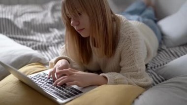 Güzel sarışın ergen, dizüstü bilgisayarla bir yatakta uzanıyor ve sohbet ediyor ya da arkadaşlarıyla mesajlaşıyor. Ev işi, sörf ya da internet konsepti üzerine sohbet..