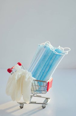 Yüz maskeli ve eldivenli küçük bir alışveriş arabası. Coronavirus (covid-19) koruyucu maske ve eldiven konseptini önleme ve satın alma.