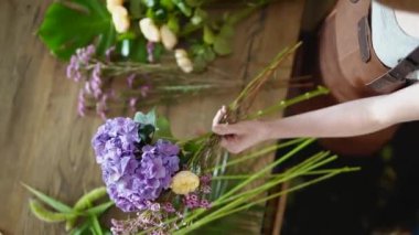 Deri önlüklü, elinde güzel kasımpatı ve gül çiçekleri olan genç bir çiçekçi dükkânda buket yapıyor. Üst Manzara. Küçük işletme ve fabrika kavramı.