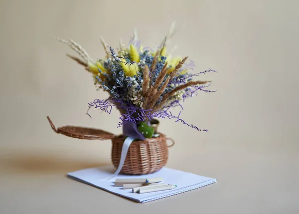 꽃들은 바구니에 꽃다발을 연필과 종이를 베이지 배경에 놓는다 지식의 — 스톡 사진