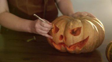 Önlüklü bir kadın keskin bir bıçakla balkabağının gözünü oyuyor ve Cadılar Bayramı için korkunç bir balkabağı feneri yapıyor. Cadılar Bayramı konsepti 4K görüntü.