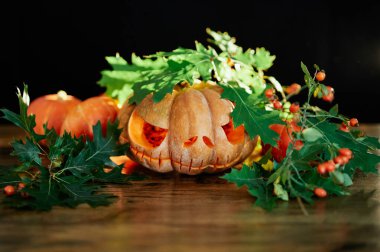 Cadılar Bayramı için oyulmuş balkabağı, koyu arkaplan ve yeşil yapraklı. İçinde mum olan taze balkabağı süslemesi. Jack O Fenerin gülen yüzü. Sonbahar Cadılar Bayramı