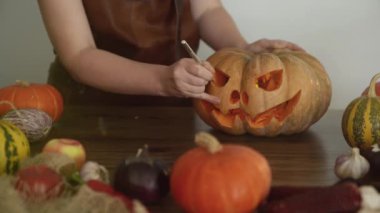 Ev hanımı Cadılar Bayramı için korkunç bir balkabağı feneri yapıyor. Önlüklü bir kadın bıçakla balkabağının gözünü oyuyor. Cadılar Bayramı konsepti 4K görüntü.