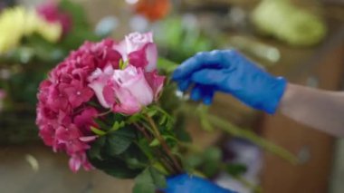 Mavi eldivenli bahçıvan kadın muhteşem bir buket kasımpatı ve gül çiçeği yapıyor. Küçük işletme konsepti. Yan görüş. 4K görüntü.
