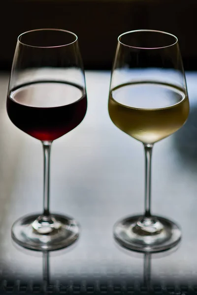 Tall glasses of red and yellow wine against black background