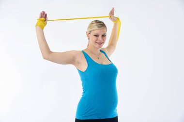 Mavi tişört blondy hamile kadında genç sarı fitness lastik bant, beyaz arka plan ile çalışmaları yapar