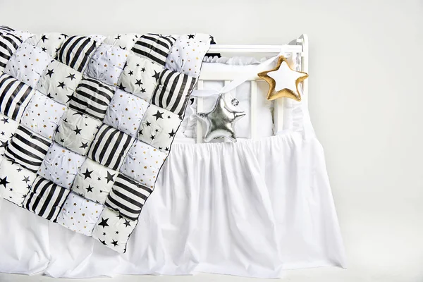 Silver and gold star shaped pillows and patchwork comforter on a white baby cot