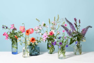 Mavi arka planda güzel kır çiçekleri olan cam vazolar.