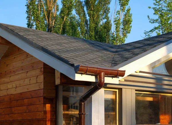 Rain gutter system with bitumen roof shingles on a wooden house.