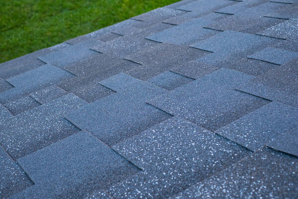 Top view of a roof made of asphalt shingles against a green lawn background