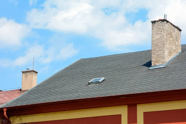 在蓝天的背景下 有天窗和雨水排水沟的沥青瓦片屋顶 房子与老烟囱 — 图库照片