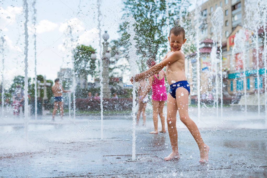Cheerful child playing in a water fountain and enjoying the cool streams of water in a summer hot day.