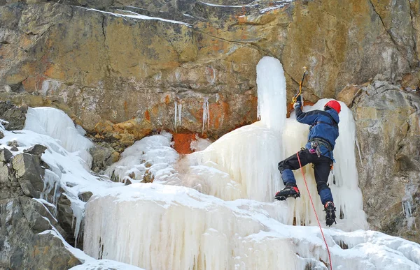 Un escalador de hielo con crampones escalando una cascada congelada —  Fotos de Stock