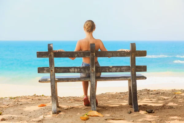 Joven hermosa chica sentado en un banco en la playa — Foto de Stock