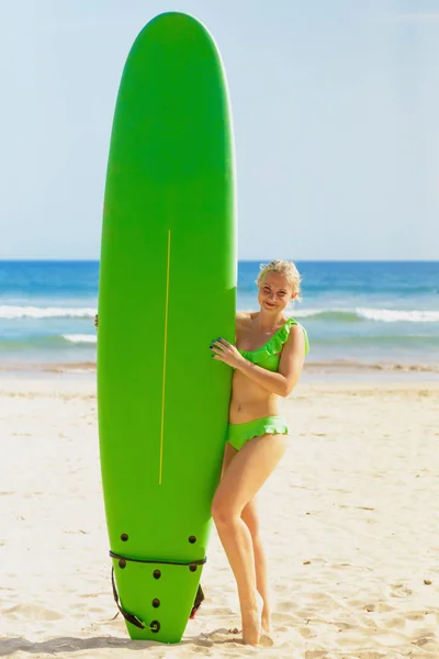 Frau im grünen Bikini posiert in der Nähe eines grünen Surfbretts — Stockfoto