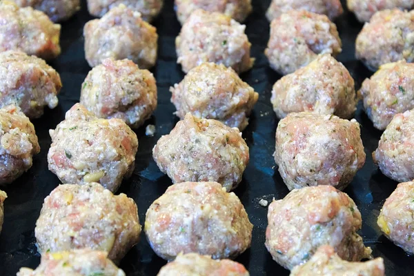 Raw turkey meatballs on a black cooking sheet