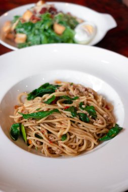Tavada kızartılmış kıyılmış domuz eti ve Tay fesleğen spagetti beyaz tabak Tay tarzı üzerinde