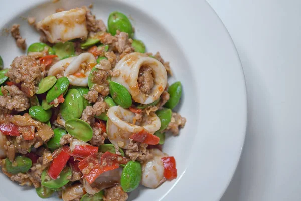 Stir-Fried Twisted Cluster Bean with squid/Bitter Bean on a White Dish Over white Table.