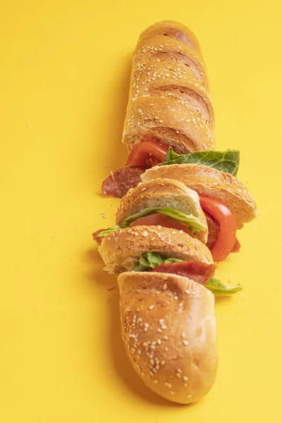 Baguette with sesame seeds, sandwich with tomato and sausage on a yellow background — Stock Photo, Image