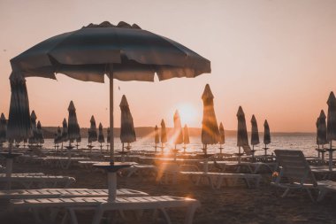 Sahilde şafak söktü. Güneş ve şemsiyeler yükselen güneşin ışınlarında. İnsanlar olmadan plaj.