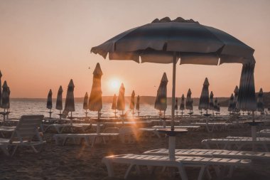 Sahilde şafak söktü. Güneş ve şemsiyeler yükselen güneşin ışınlarında. İnsanlar olmadan plaj.