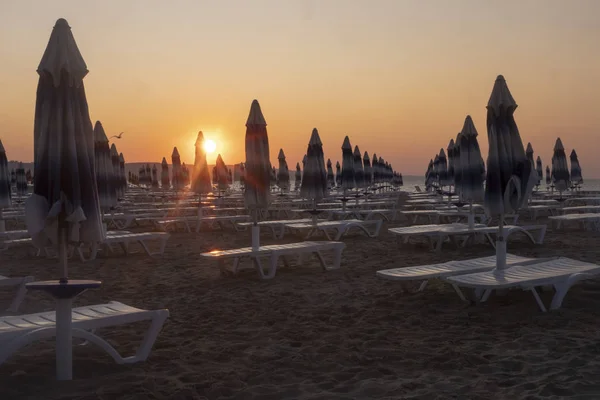 Montones de sombrillas vacías y tumbonas en la playa de la mañana al amanecer — Foto de Stock