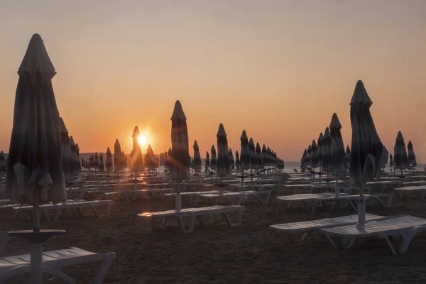 Рассвет на пляже. Солнечные шезлонги и зонтики в лучах восходящего солнца. Пляж без людей . — стоковое фото