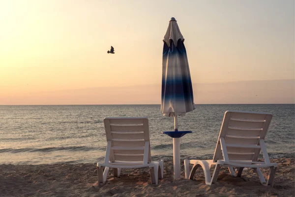 Amanhecer na praia. Espreguiçadeiras e guarda-sóis nos raios do sol nascente. Praia sem pessoas . — Fotografia de Stock