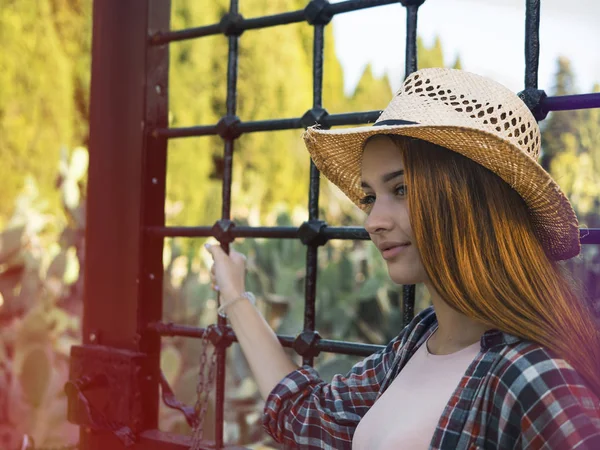 Молодая рыжая женщина на ранчо в соломенной шляпе, клетчатая рубашка и джинсы на заднем плане гриля. Случайный стиль — стоковое фото