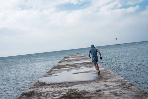 Male athlete runs on the pier against the background of the sea — Stock Photo, Image