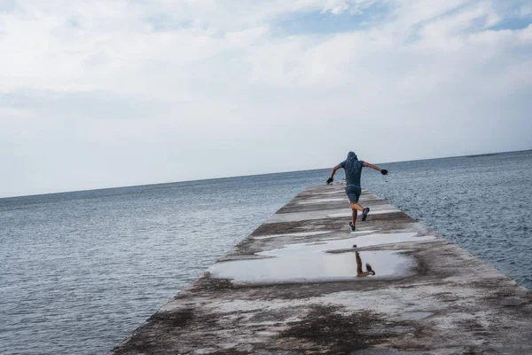 Мужской спортсмен бегает по пирсу на фоне моря — стоковое фото