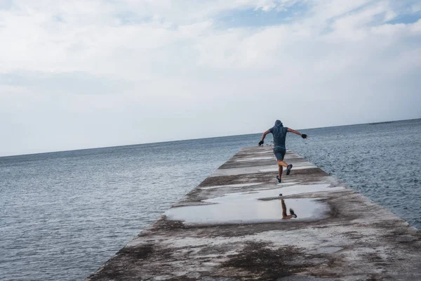 Male athlete runs on the pier against the background of the sea — Stock Photo, Image