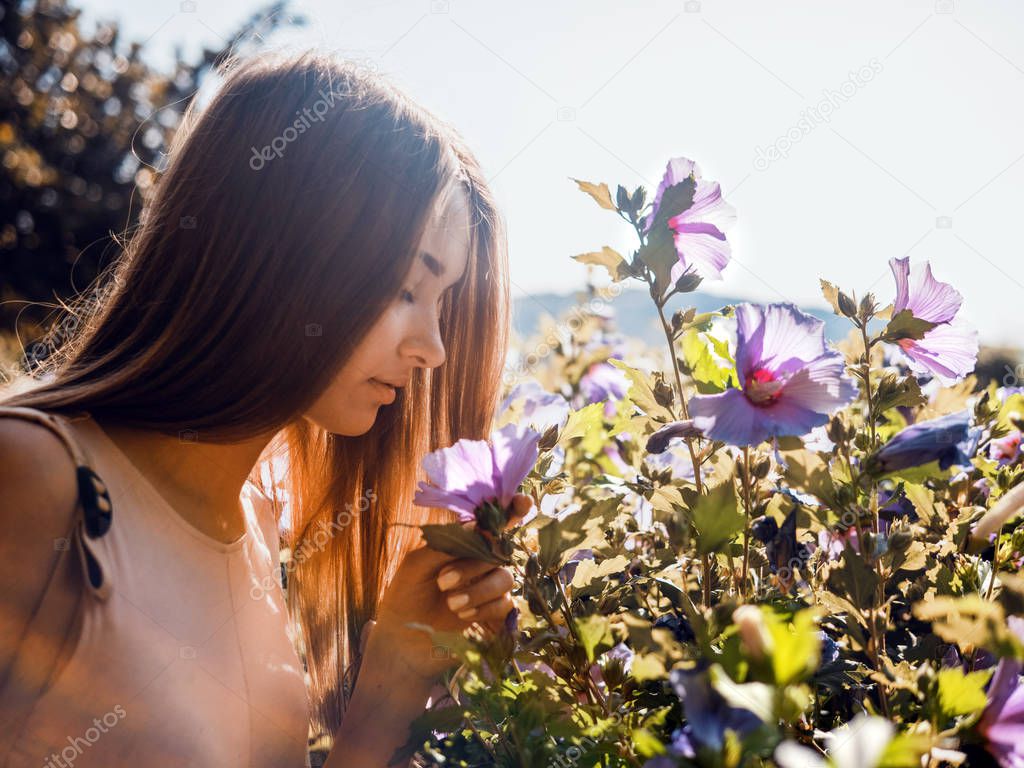 Beautiful young woman sniffing flowers in the garden