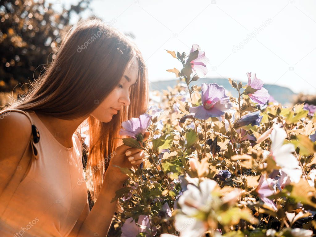 Beautiful young woman sniffing flowers in the garden