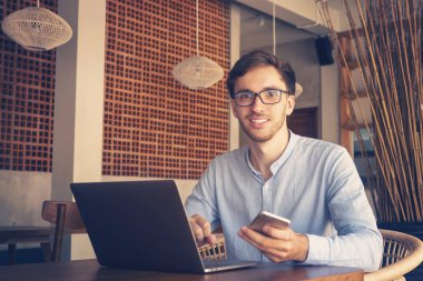 Kafede smartphone ve dizüstü bilgisayar kullanan mutlu casual adam
