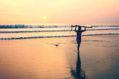 Endonezya, Bali, Nisan 4, 2019 Sörf tahtası ile bir kız gün batımında denizden çıkıyor