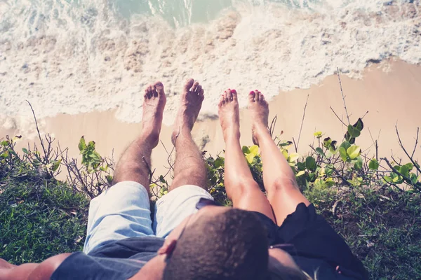 Um homem e uma mulher penduraram as pernas na beira de um penhasco, sentados acima do oceano. . — Fotografia de Stock