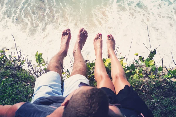 Um homem e uma mulher penduraram as pernas na beira de um penhasco, sentados acima do oceano. . — Fotografia de Stock