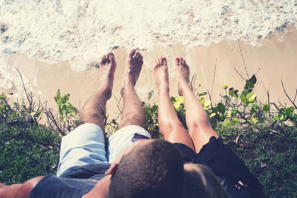 Ένας άντρας και μια γυναίκα κρέμασαν τα πόδια της στην άκρη ενός γκρεμού κάθεται πάνω από τον ωκεανό. — Φωτογραφία Αρχείου