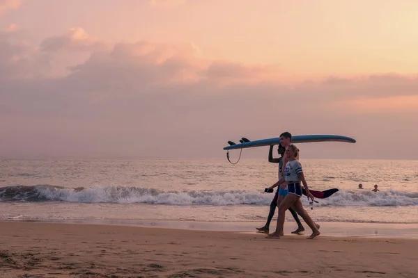 Sri Lanka Hikkaduwa febrero 8, 2019 Una compañía de personas surfistas van con una tabla en la playa al atardecer — Foto de Stock